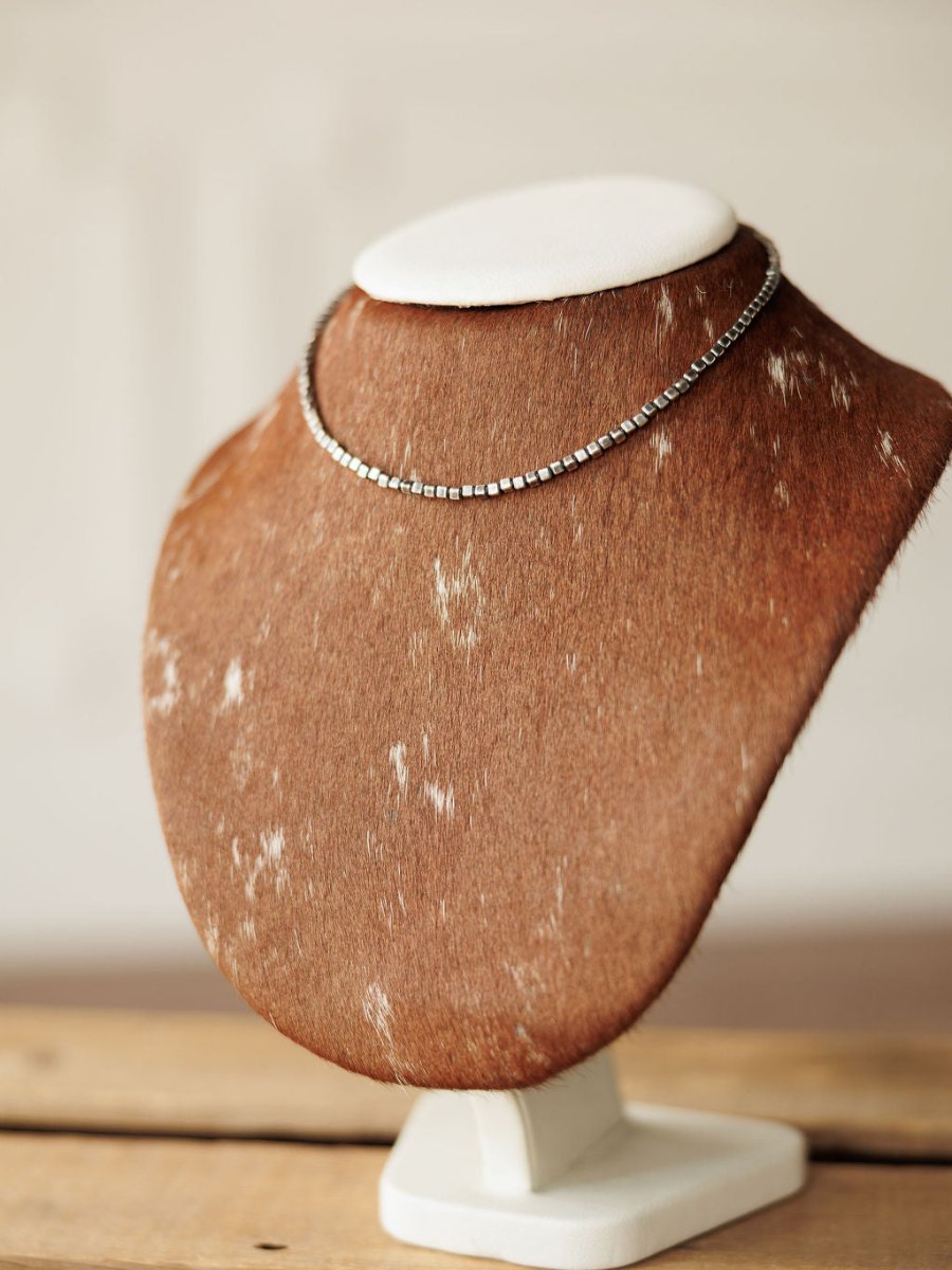 The Atoka Necklace by Savannah Sevens western life{&}style, a simple sterling silver chain, is displayed on a brown and white speckled fur-covered jewelry stand with a white top, set on a wooden surface.