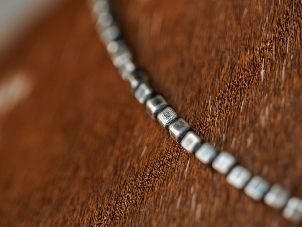 The Atoka Necklace by Savannah Sevens western life{&}style features sterling silver Navajo pearls, shown in sharp focus as they drape across a textured brown leather surface with a softly blurred background.