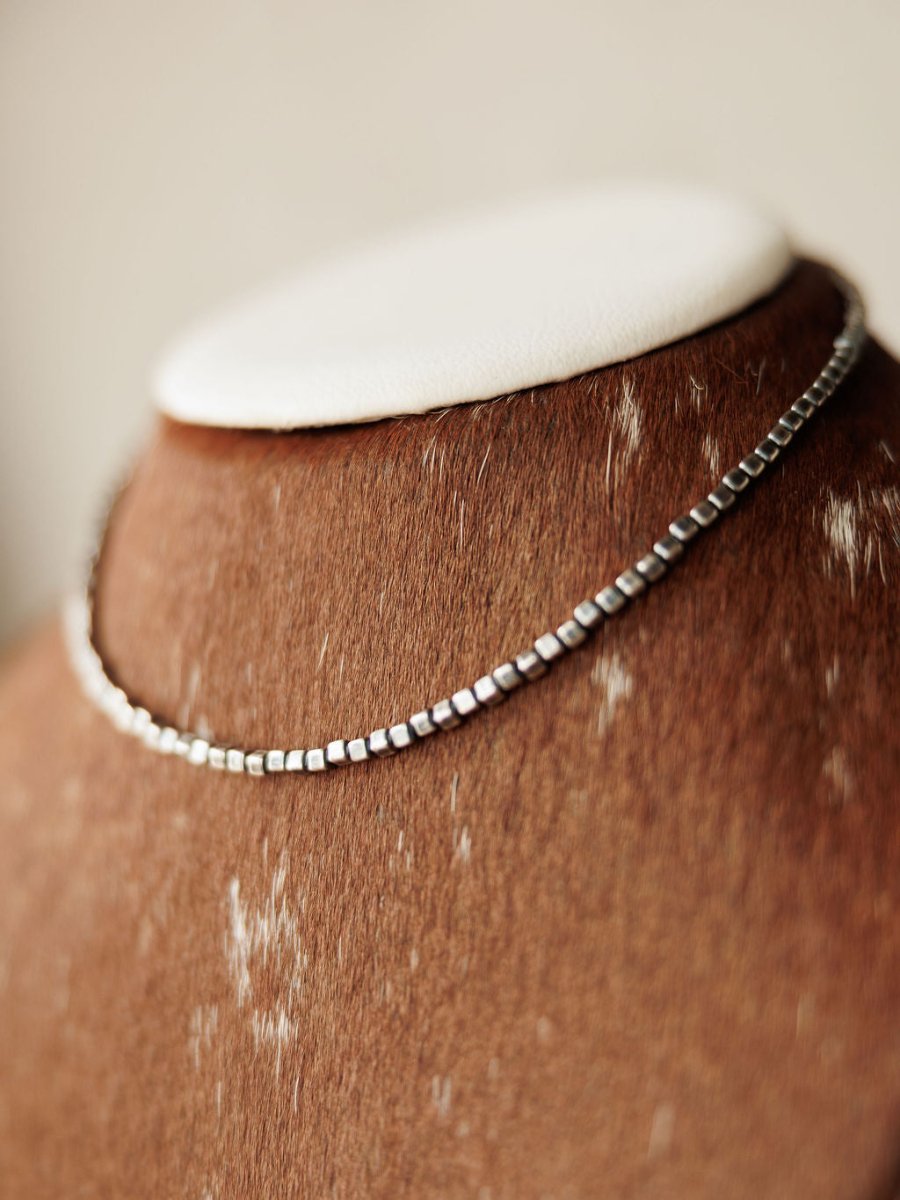 The Atoka Necklace by Savannah Sevens western life{&}style, a sterling silver box chain, is displayed on a brown cowhide-textured jewelry bust with white patches and a white top.