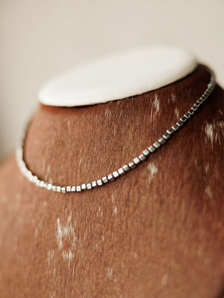 The Atoka Necklace by Savannah Sevens western life{&}style, a sterling silver box chain, is displayed on a brown cowhide-textured jewelry bust with white patches and a white top.
