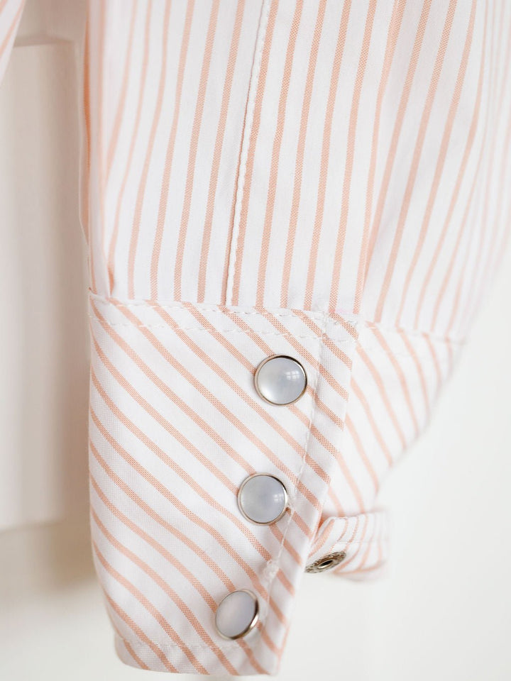 Close-up of the Aullville Striped Pearl Snap Top by Savannah Sevens western life{&}style, featuring a snap button cuff with light pink and white vertical stripes, three shiny pearl snaps, and a diagonally patterned cuff for a unique retro western look.