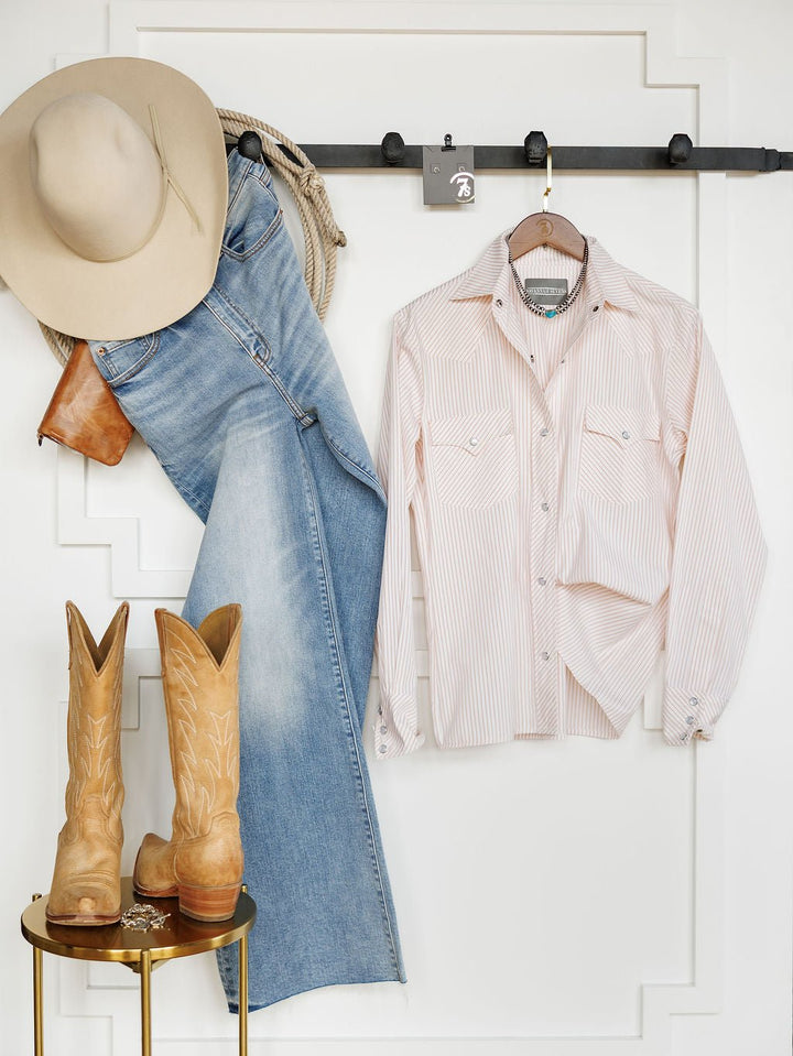 Aullville Striped Pearl Snap Top by Savannah Sevens western life{&}style is displayed with a beige cowboy hat, light brown boots, blue jeans, a brown belt, and coiled rope on a white wall with a black rack for a classic Western look.