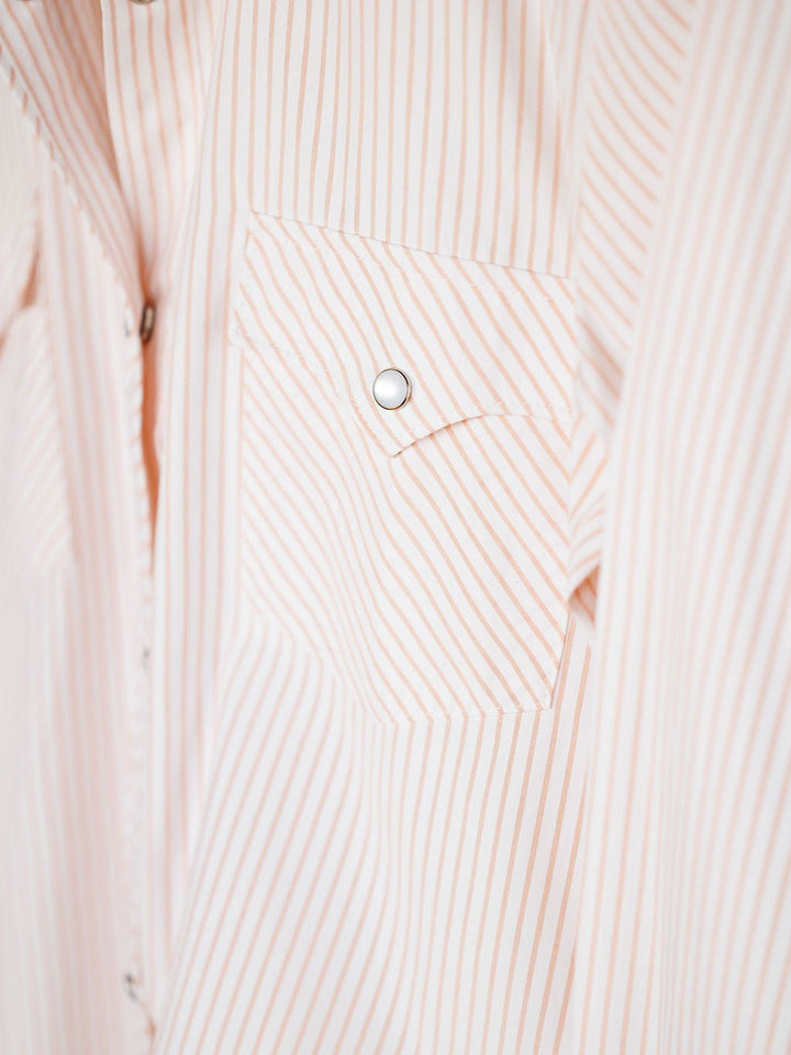 Close-up of the Savannah Sevens western life{&}style Aullville Striped Pearl Snap Top, featuring vertical and diagonal peach stripes, a buttoned chest pocket, and visible pearl snaps. This long sleeve shirt lends vintage western flair to your wardrobe.