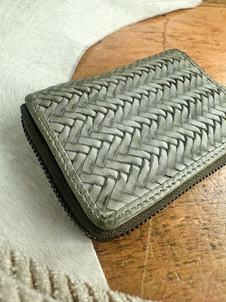 The Avoca Wallet by Savannah Sevens western life{&}style, a small woven genuine leather zip wallet, is displayed on a wooden surface with white fur in the background.