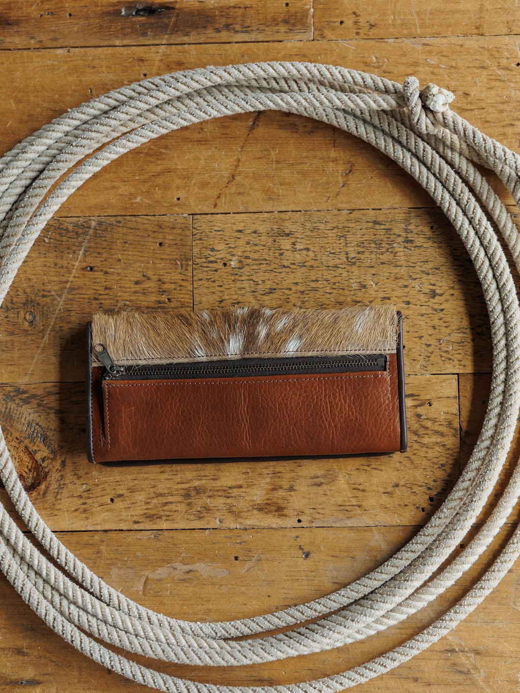 A Savannah Sevens western life{&}style Axis Bison Leather Cognac Wallet sits on a wooden surface, centered within a coiled white rope.