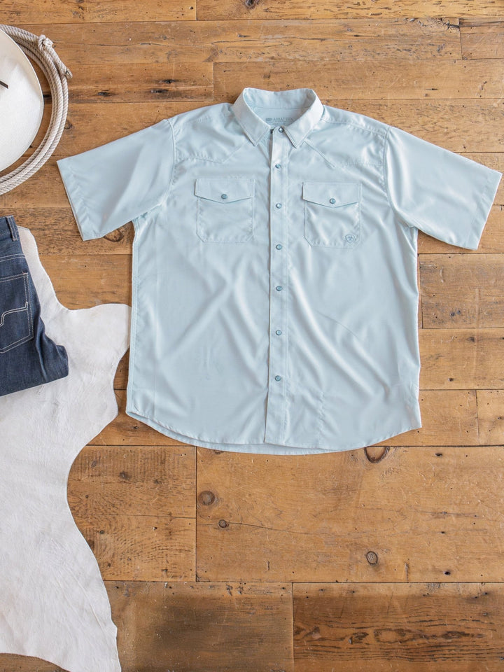 A Barlett Ariat Men's Light Seafoam Pearl Snap shirt from Savannah Sevens western life{&}style is laid flat on a wooden floor next to dark jeans, a white cowboy hat, brown boots, and a white cowhide rug—offering sun protection and western style.