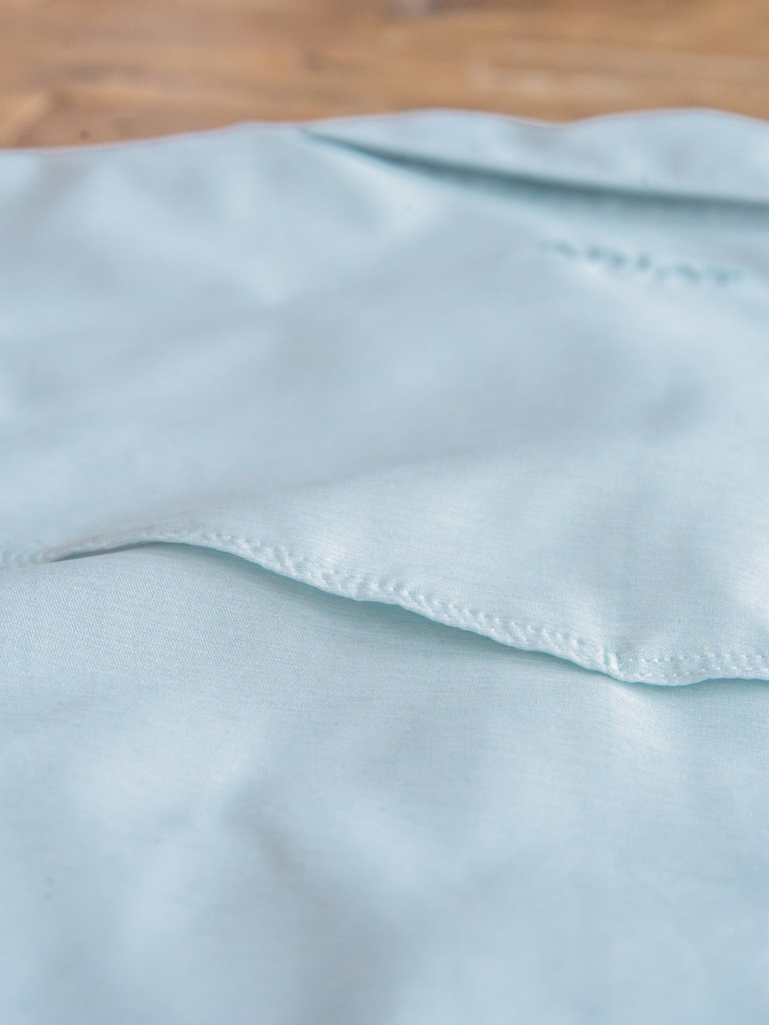 A close-up of the Barlett Ariat Men's Light Seafoam Pearl Snap shirt fabric by Savannah Sevens western life{&}style, showing visible seams and stitching, laid flat on a wooden surface.
