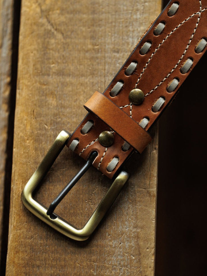 The Barlow Belt by Savannah Sevens western life{&}style features white buck stitch detail, metal rivets, and a brass interchangeable buckle, shown close-up on a wooden surface.