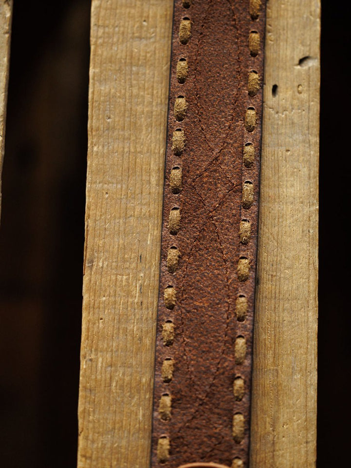 Close-up of the Barlow Belt by Savannah Sevens western life{&}style—a weathered brown leather belt with visible buck stitch detail, shown vertically on a textured, grooved wooden surface.