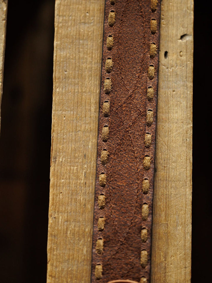 Close-up of the Barlow Belt by Savannah Sevens western life{&}style—a weathered brown leather belt with visible buck stitch detail, shown vertically on a textured, grooved wooden surface.