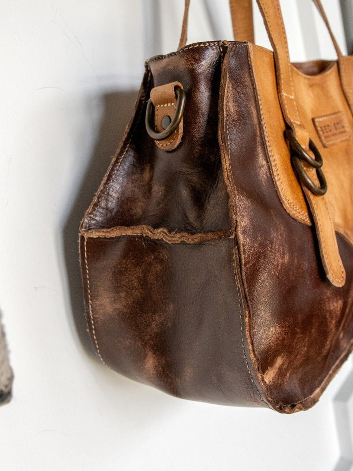 A close-up of the Barstow Leather Handbag by Savannah Sevens western life{&}style showcases the distressed leather, visible stitching, and metal rings, emphasizing the worn texture on the side and bottom panels.