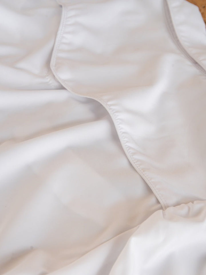 A close-up of the Belington White Retro Pearl Snap Top by Savannah Sevens western life{&}style showcases its white fabric with soft folds and curved stitched edges, creating a smooth and slightly wavy texture.