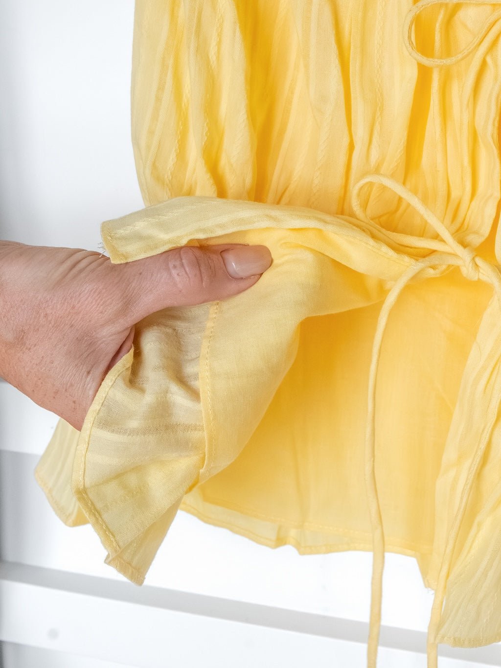 A hand holds the edge of the Bella Villa Yellow Tie Front Top by Savannah Sevens western life{&}style, a sheer piece with a gathered waist and delicate detailing.