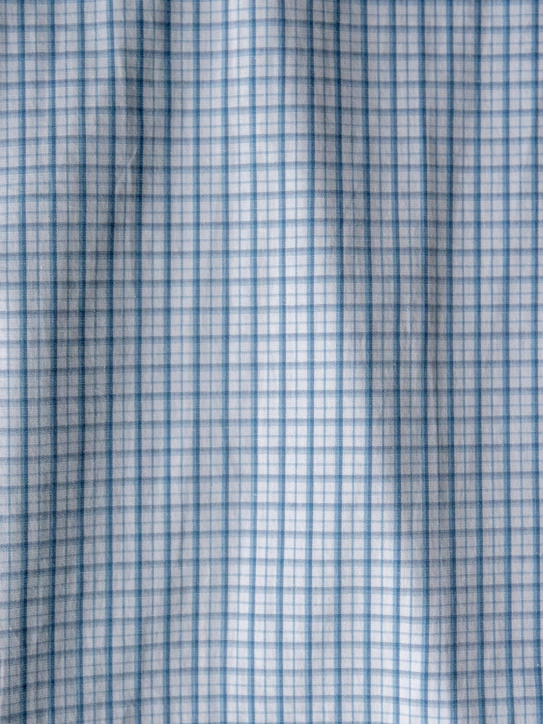 Close-up of the soft, slightly wrinkled blue plaid fabric on the Bentonville Wrangler Men's Blue Plaid Button Up by Savannah Sevens western life{&}style. Features a light blue and white checkered grid pattern.