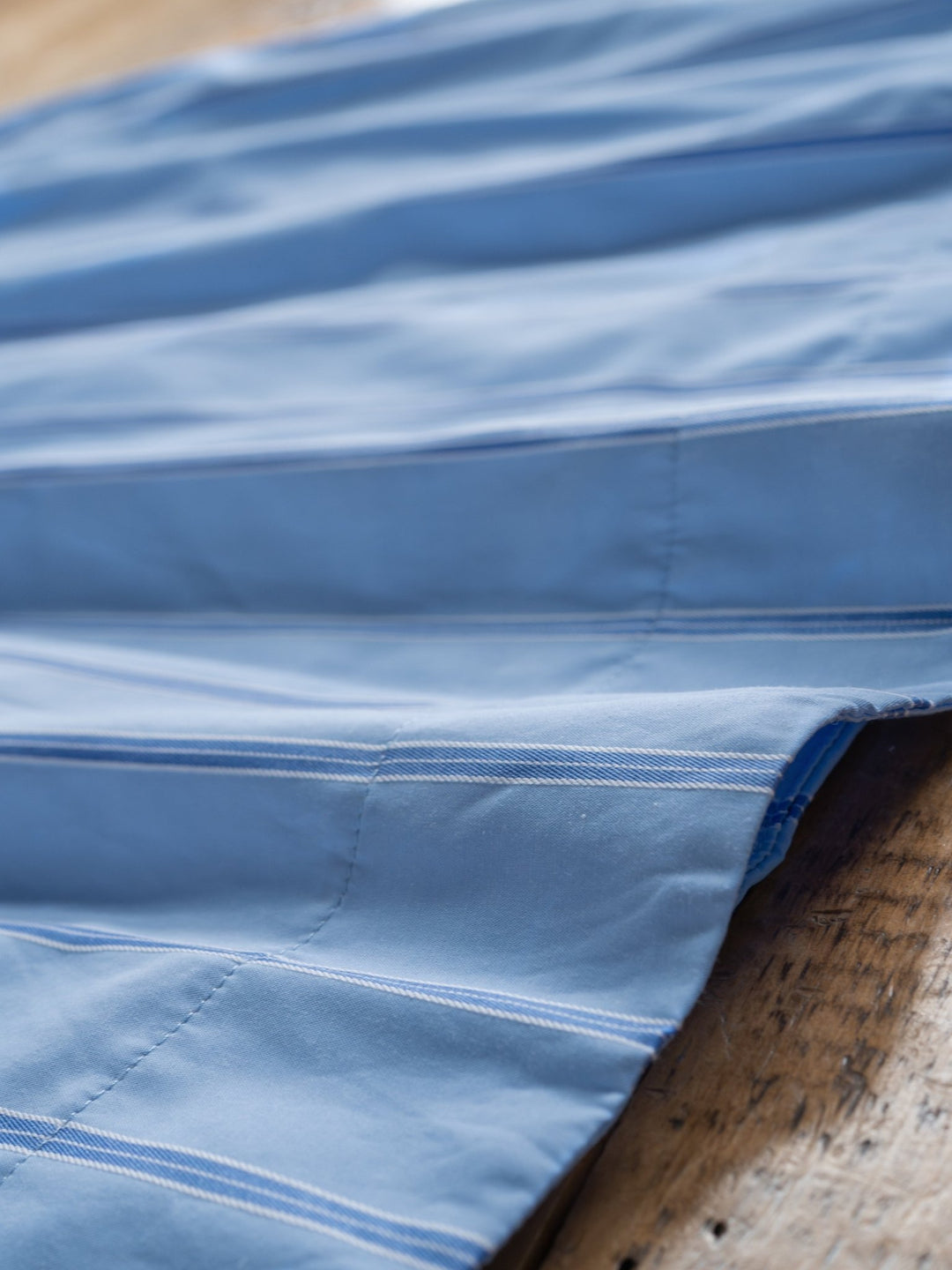 A close-up of The Berkeley by Savannah Sevens western life{&}style shows its blue striped fabric with white stitching, neatly sewn seams, and parallel lines, draped over a wooden surface.