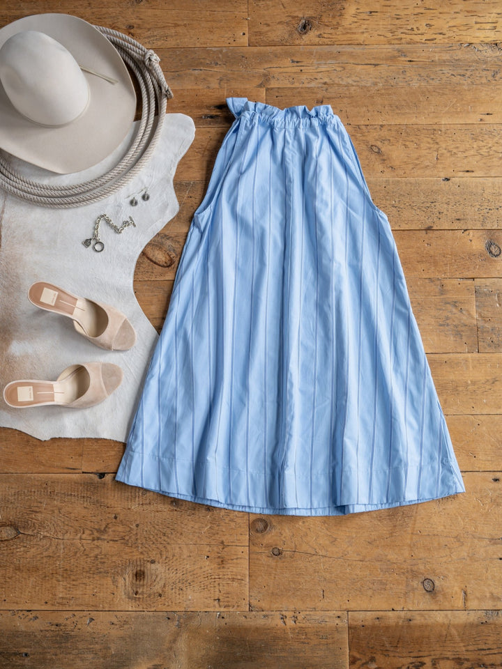 The Berkeley dress by Savannah Sevens western life{&}style is displayed on a wooden floor beside beige heels, a wide-brimmed hat, necklace, and earrings, all styled atop a white fur rug with a coiled rope.
