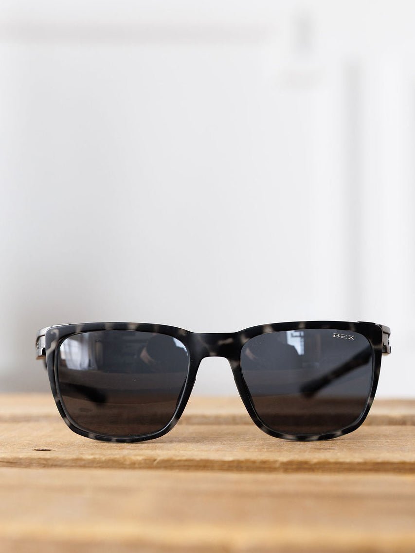 The Bex Adams Sunglasses {Tortoise Gray} by Savannah Sevens western life{&}style, featuring polarized lenses and UV protection, rest on a wooden surface with a white background.