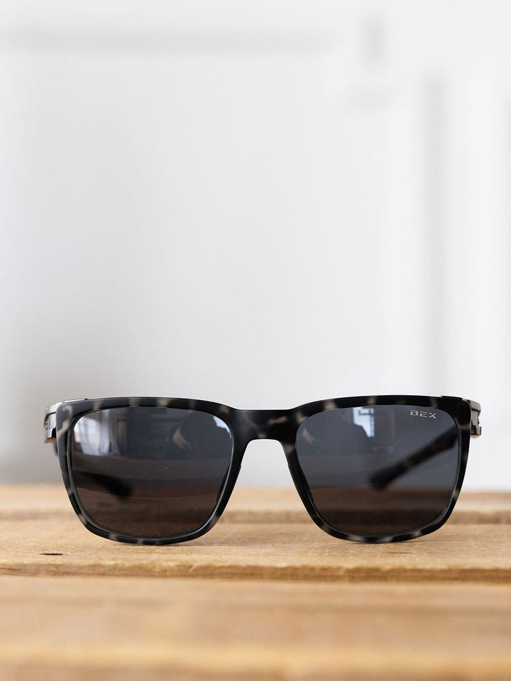 The Bex Adams Sunglasses {Tortoise Gray} by Savannah Sevens western life{&}style, featuring polarized lenses and UV protection, rest on a wooden surface with a white background.