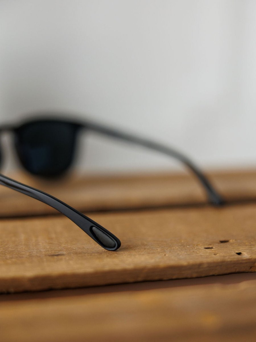Close-up of Bex Zion Sunglasses {Black} by Savannah Sevens western life{&}style with scratch-resistant polarized lenses, focusing on the temples as they rest on a wooden surface, blurred lenses in the background.