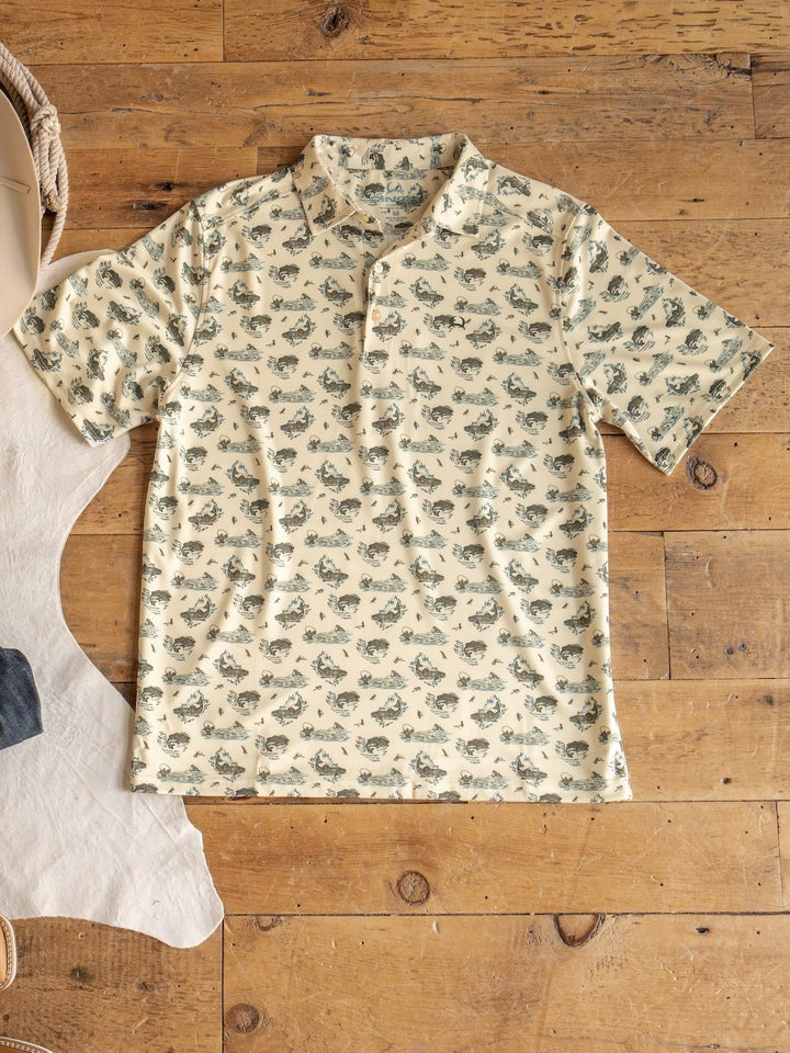 The Big Bass Cinch Men's Graphic Polo by Savannah Sevens western life{&}style—a beige short-sleeve ArenaFlex shirt with an all-over fish print—is laid flat on a wooden floor beside part of a white rug and some denim fabric. This polo features moisture-wicking fabric to keep you comfortable.