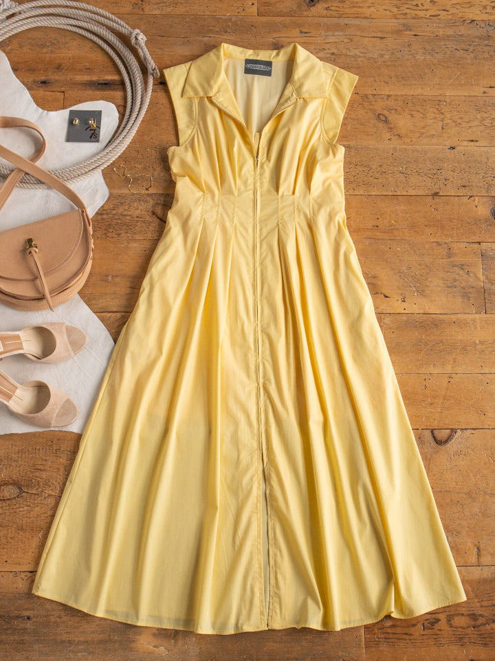 The Biloxi Butter Zip Front Dress by Savannah Sevens western life{&}style is displayed on a wooden floor, paired with beige sandals, a light tan crossbody bag, a white cloth, and earrings.