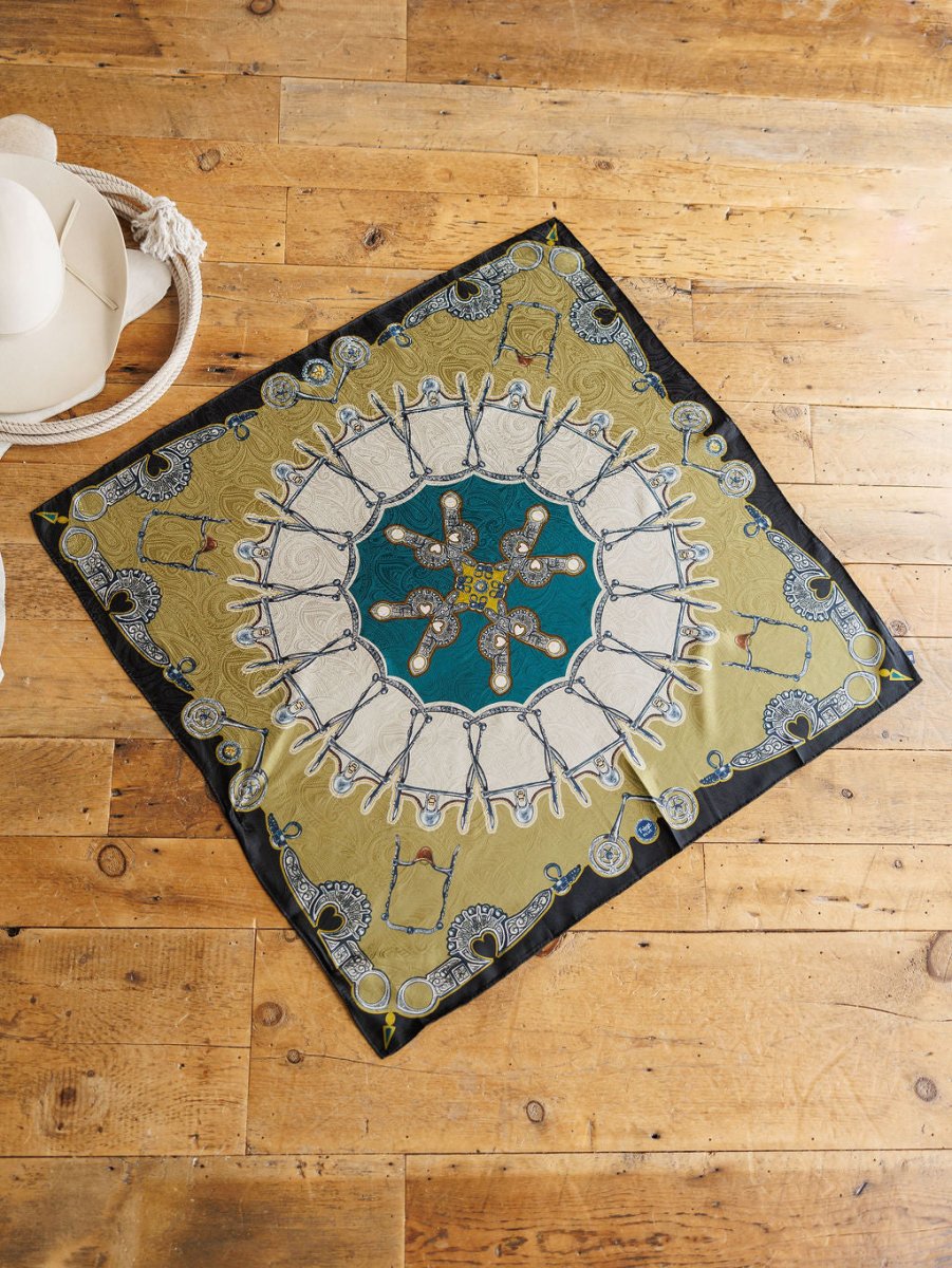 The Bits Wild Rag {Teal} by Savannah Sevens western life{&}style, a luxurious paisley silk scarf in gold, black, and teal, is displayed on a wooden floor beside a white wide-brim hat and coiled rope.