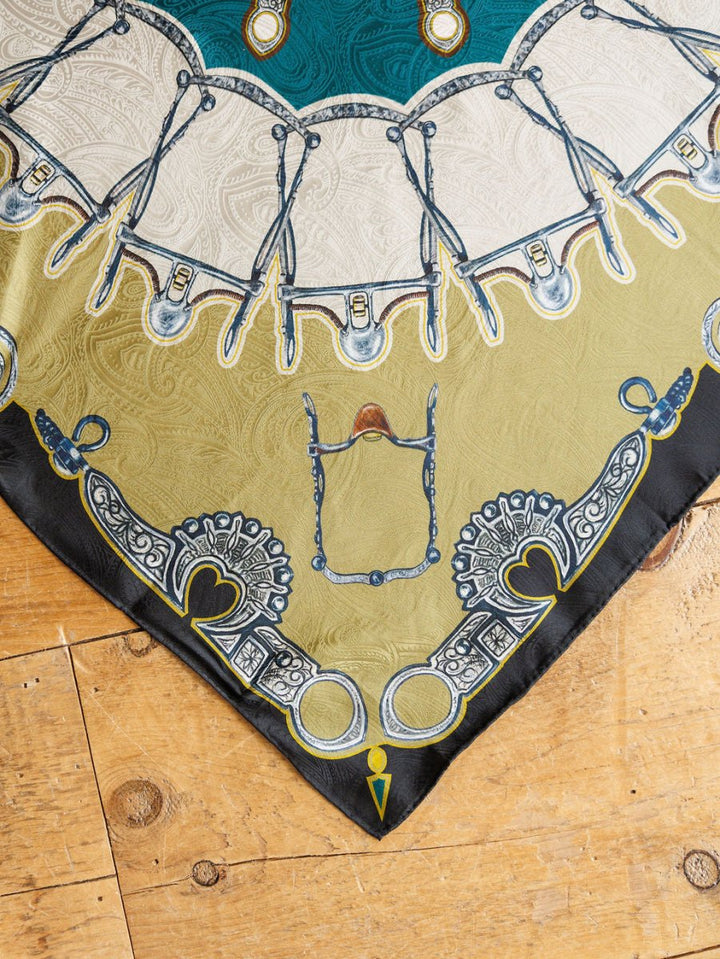The Bits Wild Rag {Teal} by Savannah Sevens western life{&}style features ornate gold, cream, and teal bridles, bits, and hearts on jacquard silk with a black border, displayed on a wooden floor for classic western style.