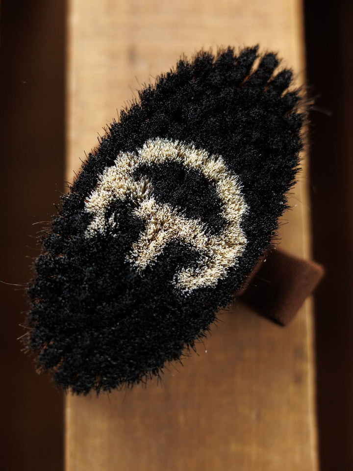 A close-up of the Blanket Brush by Savannah Sevens western life{&}style shows its textured, oval-shaped black surface with a white crescent and vertical line design on wood—craftsmanship as refined as luxury blankets.