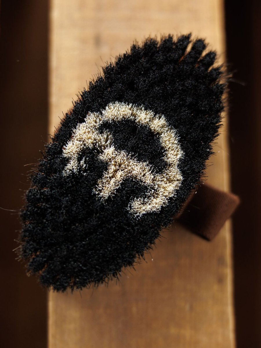 A close-up of the Blanket Brush by Savannah Sevens western life{&}style shows its textured, oval-shaped black surface with a white crescent and vertical line design on wood—craftsmanship as refined as luxury blankets.