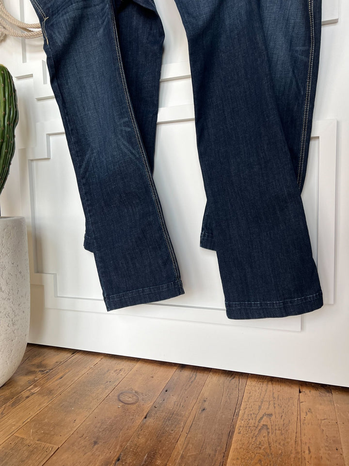 The Blayze Perfect Rise Trouser Jean *Exclusive* by Savannah Sevens western life{&}style in medium dark wash denim hangs against a white paneled wall with a plant in a white pot and wooden floorboards. Features a comfy no-gap waist.