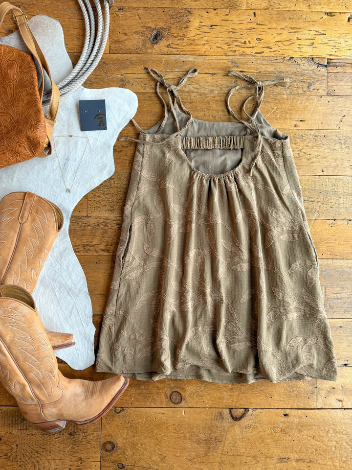 The Bluff City Sage Floral Dress by Savannah Sevens western life{&}style is displayed on a wooden floor with tan cowboy boots, a brown leather bag, silver necklace, western belt, and grey hat.