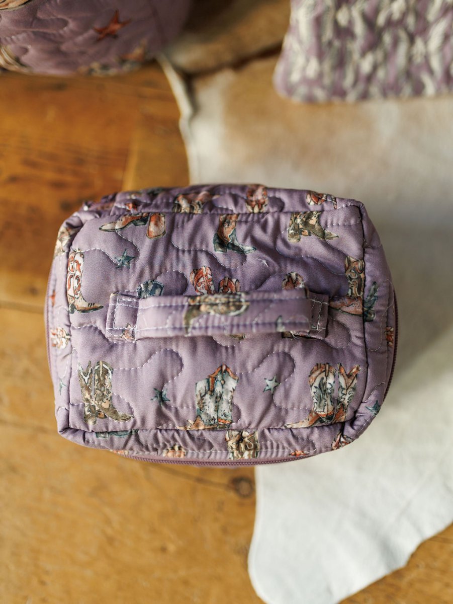 The Boots {Collection} by Savannah Sevens western life{&}style features a quilted purple bag set with whimsical animal prints, visible stitching, and a handled pouch, highlighting its handmade charm on a wooden surface beside a white cloth.