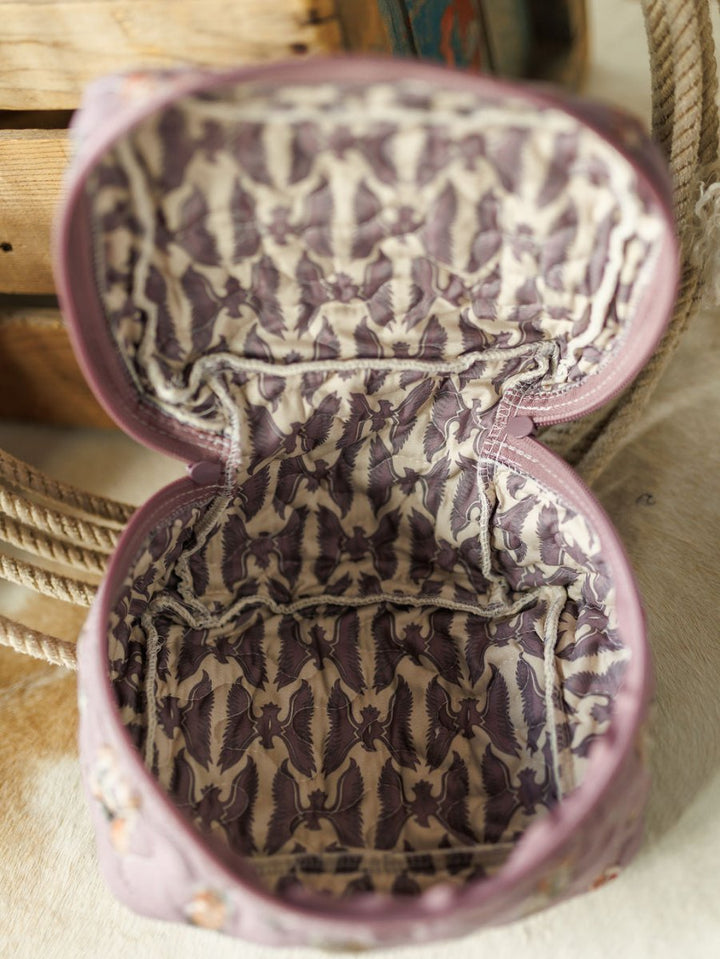 Open, empty fabric pouch from the Boots Collection by Savannah Sevens western life{&}style, with a light purple interior and dark purple birds in flight pattern. Part of a quilted bag set, displayed on cream surface beside rope and wooden boxes.