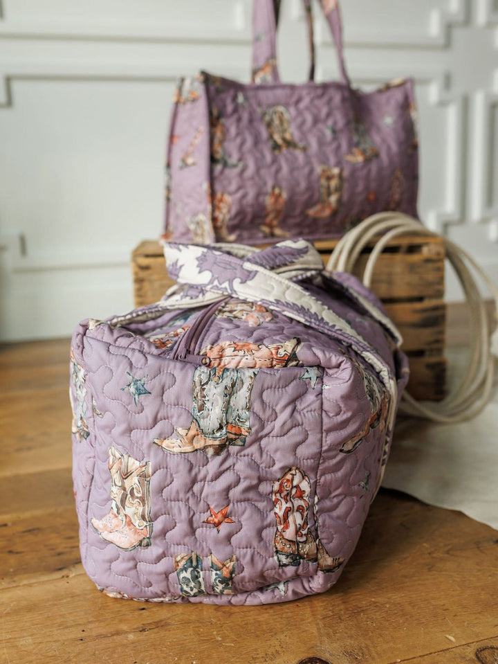 Two handmade quilt bags from the Boots {Collection} by Savannah Sevens western life{&}style with colorful boot patterns rest on a wooden floor, one in front and the other behind near a decorative wooden box.