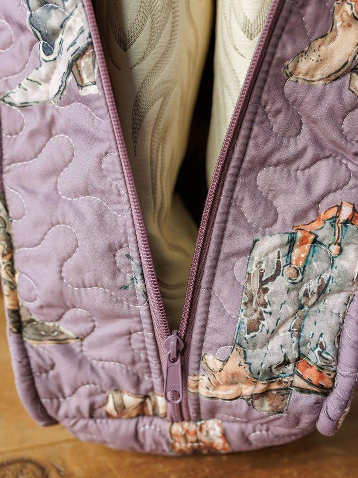 Close-up of a quilted bag from the Boots Collection by Savannah Sevens western life{&}style, featuring cowboy boots and hats on a purple background with a purple zipper. The bag is partially open, showing cream-colored contents inside.