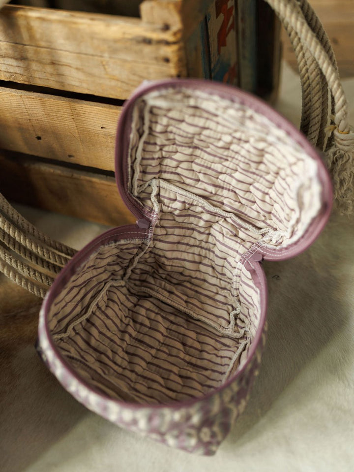 A purple, fabric-lined zippered pouch from the Boots Collection by Savannah Sevens western life{&}style rests on a light surface near a wooden crate and coiled rope, featuring a stitched striped interior inspired by handmade quilts.