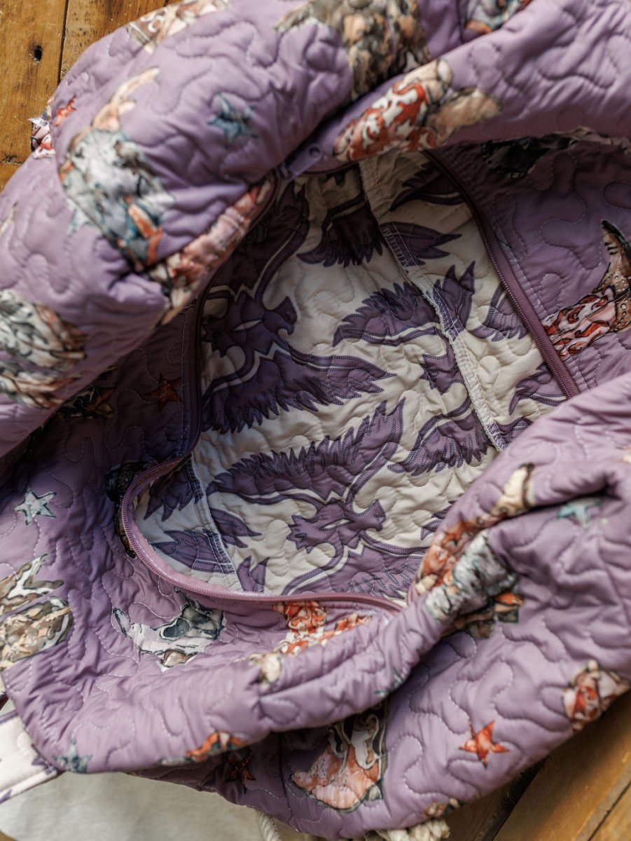 A close-up of the handmade quilted lavender bag from the Savannah Sevens western life{&}style Boots {Collection}, featuring a mountain and tree print lining in muted tones, zipper closure, and displayed on a wooden surface.