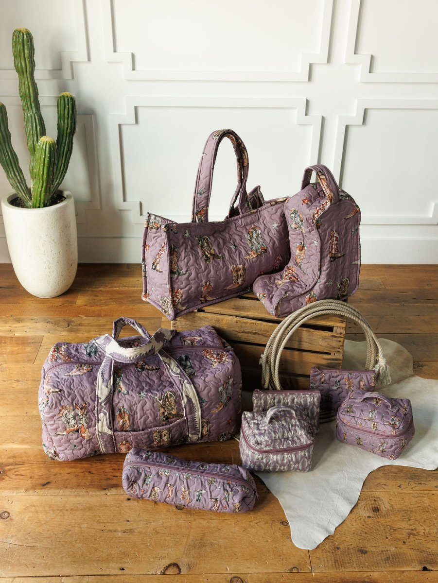 The Boots {Collection} by Savannah Sevens western life{&}style features purple quilted bag sets with embroidered animals, displayed on a wooden floor beside a cactus and white wall, highlighting this handmade quilted western travel set.
