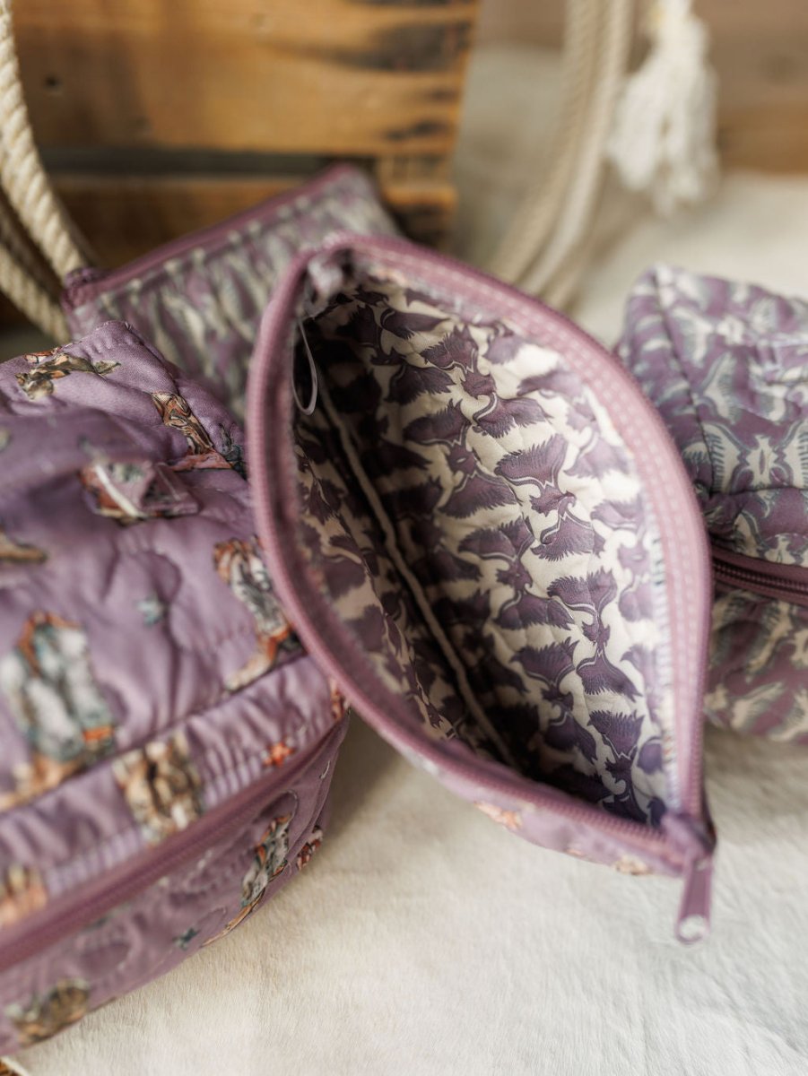 A close-up of a purple zippered pouch from the Boots Collection by Savannah Sevens western life{&}style, featuring an animal print exterior and patterned lining, displayed on a light surface with other bags and a rope handle nearby.