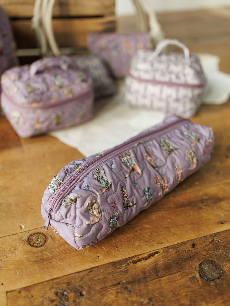 A playful cat-print quilted lavender pencil case from the Boots Collection by Savannah Sevens western life{&}style sits on a wooden table, part of a charming quilted bag set with matching handmade quilts and a white cloth in the background.