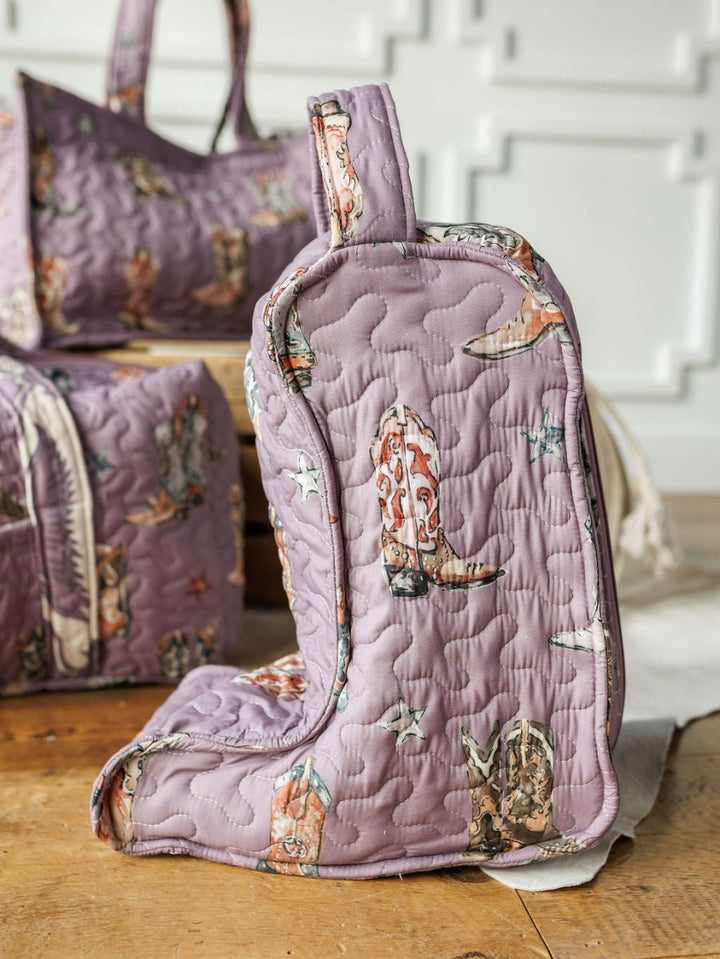 The Savannah Sevens western life{&}style Boots {Collection} quilted lavender boot bag, with a cowboy boot and star design, stands on a wooden floor alongside matching bags against a white wall.