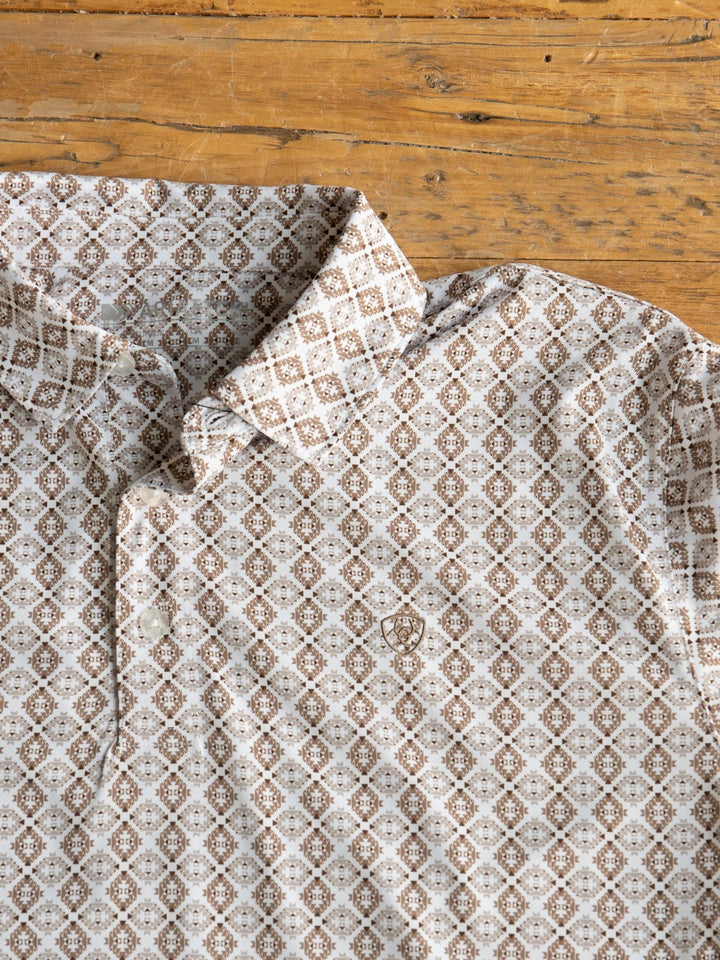 A close-up of the Bozeman Ariat Men's Southwest Polo by Savannah Sevens western life{&}style in beige and brown with a subtle chest crest and moisture-wicking fabric, laid flat on rustic wood.