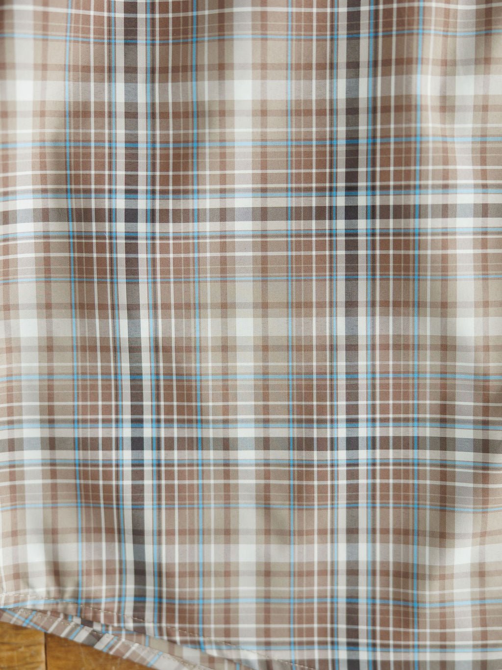 A close-up of the Brimson Ariat Men's Plaid Button Up by Savannah Sevens western life{&}style, featuring intersecting vertical and horizontal lines in brown, beige, white, and light blue.