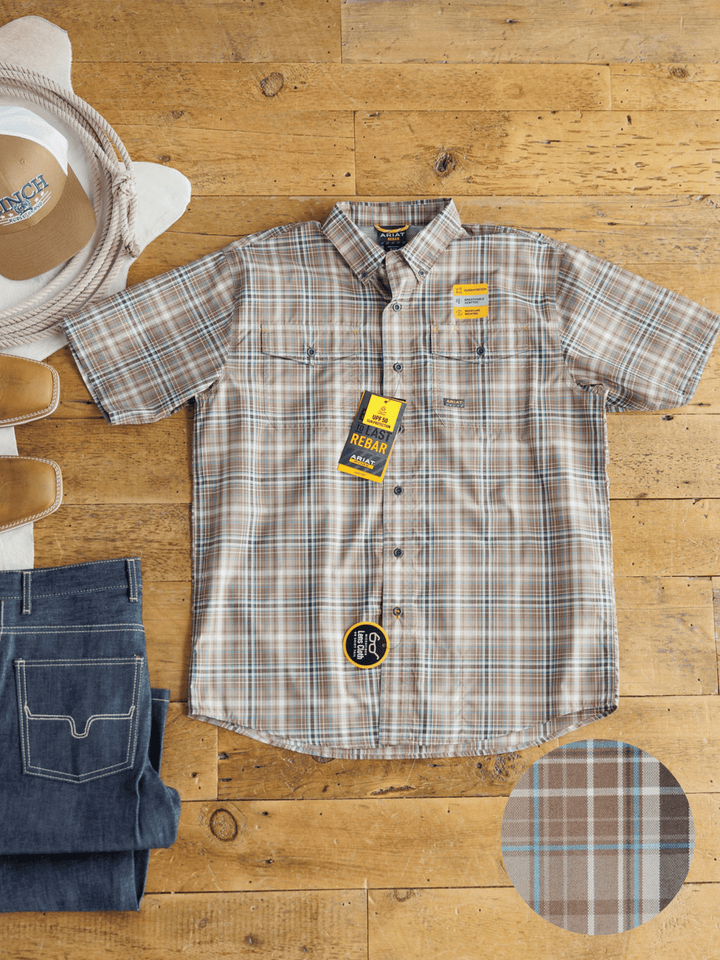 The Brimson Ariat Men's Plaid Button Up by Savannah Sevens western life{&}style is displayed flat on a wooden floor with jeans, brown shoes, and a white hat. A close-up of its plaid pattern features in the bottom right corner.