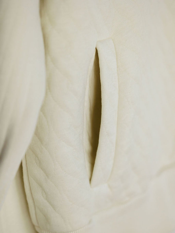 Close-up of the Britton Ivory Quilted Pullover by Savannah Sevens western life{&}style, showing its soft cream-colored fabric, detailed stitching, and vertical slit pocket.