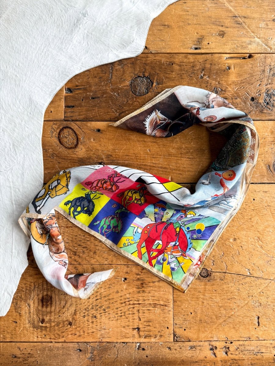 The Bronc Neck Scarf by Savannah Sevens western life{&}style, featuring a colorful pattern, is styled in a loose heart shape on rustic wood beside white textured fabric in the top left corner.