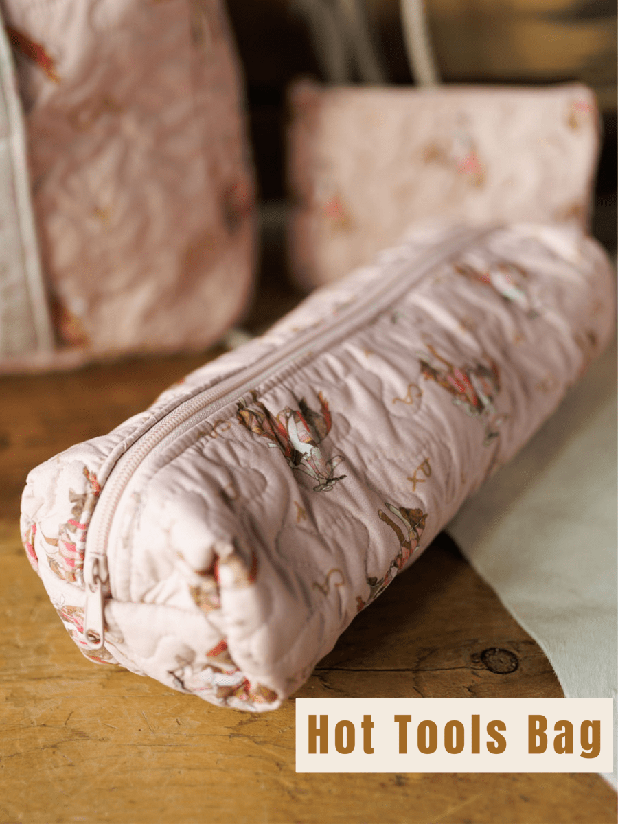 A pink quilted bag with a floral pattern and zipper from the Brumby Rose Collection by Savannah Sevens western life&style is displayed on a tabletop, with matching accessories in the background.