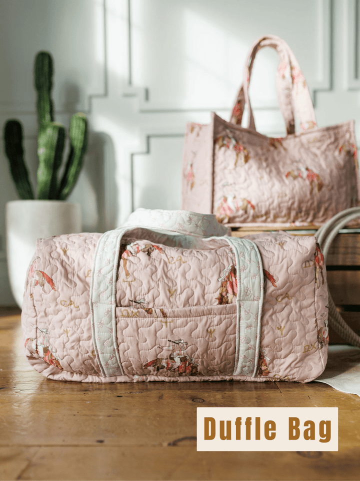 A light pink, quilted Brumby Rose duffle bag from Savannah Sevens western life & style sits on a wooden floor with floral patterns, a matching tote, and a potted cactus. "Duffle Bag" is displayed in the bottom right corner.