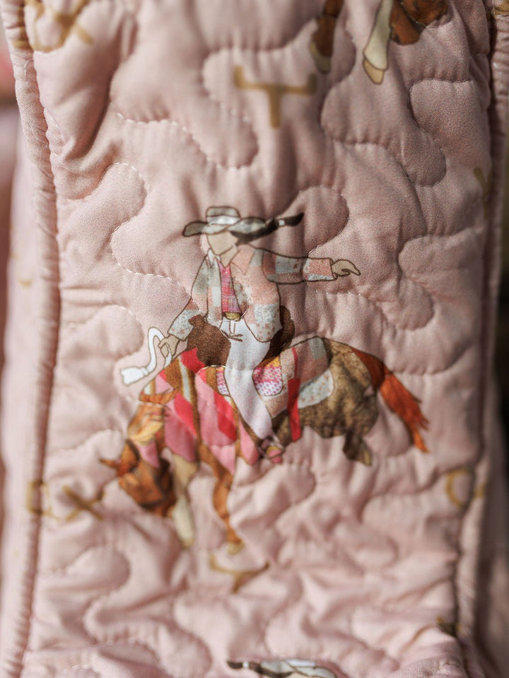 Close-up of quilted pink fabric from the Brumby Rose Collection by Savannah Sevens western life{&}style, featuring a cowboy-on-horse print with intricate stitching in soft brown, beige, and red tones.