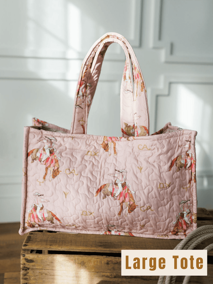 The Brumby Rose large quilted pink tote from Savannah Sevens western life{&}style features a horse and rider print. Sunlight streams onto the bag resting on wood, with “Large Tote” labeled in a beige box at the bottom right.